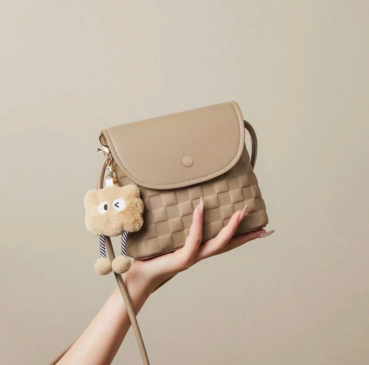 Beige mini crossbody bag with woven texture and plush keychain charm.