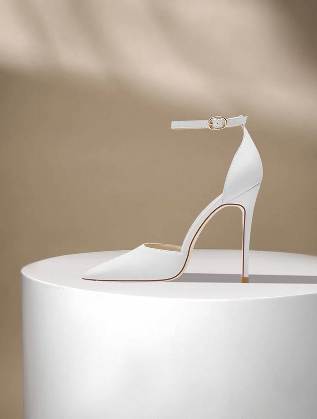 White leather stiletto heel with pointed toe and ankle strap on white platform.
