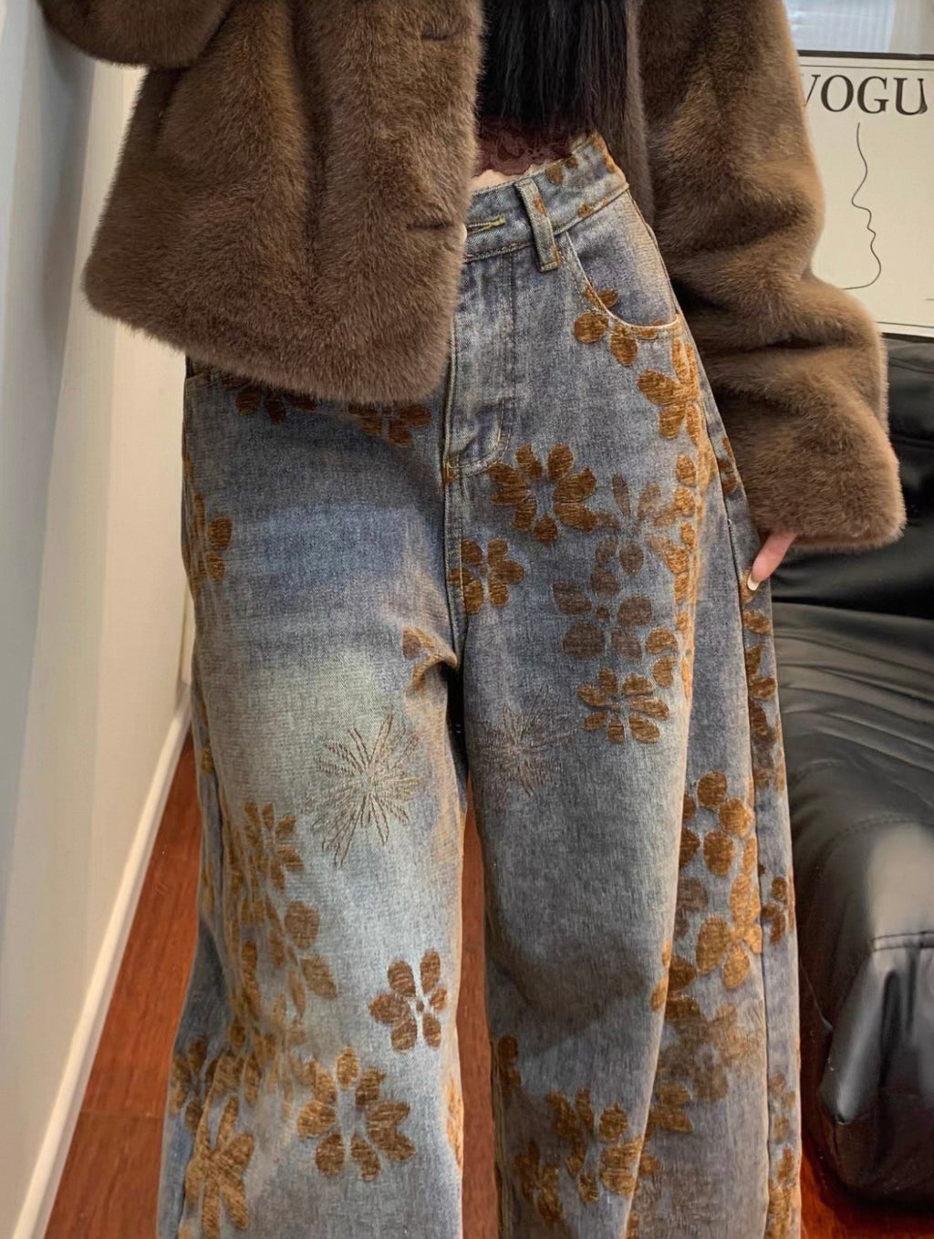 Person wearing a brown coat and jeans with floral embroidery, standing indoors.
