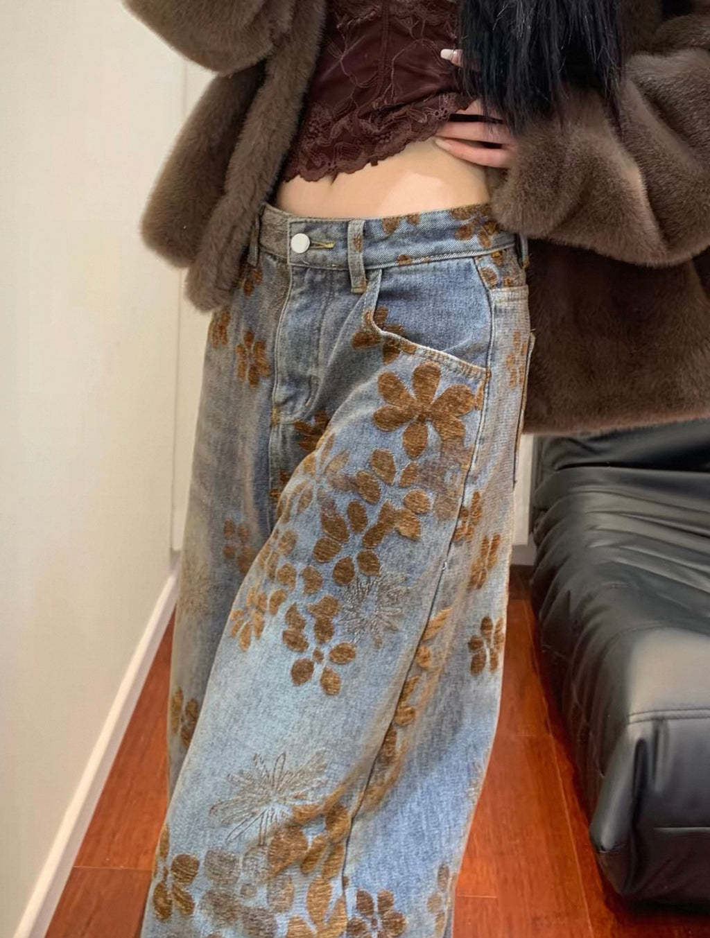 Person wearing a brown textured top and floral jeans indoors.