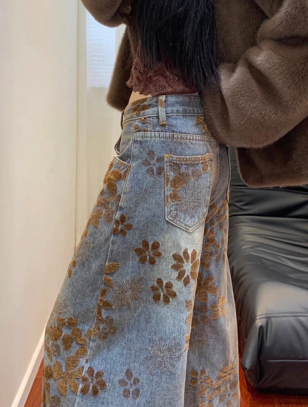Person wearing a floral-patterned denim skirt with a brown jacket indoors.