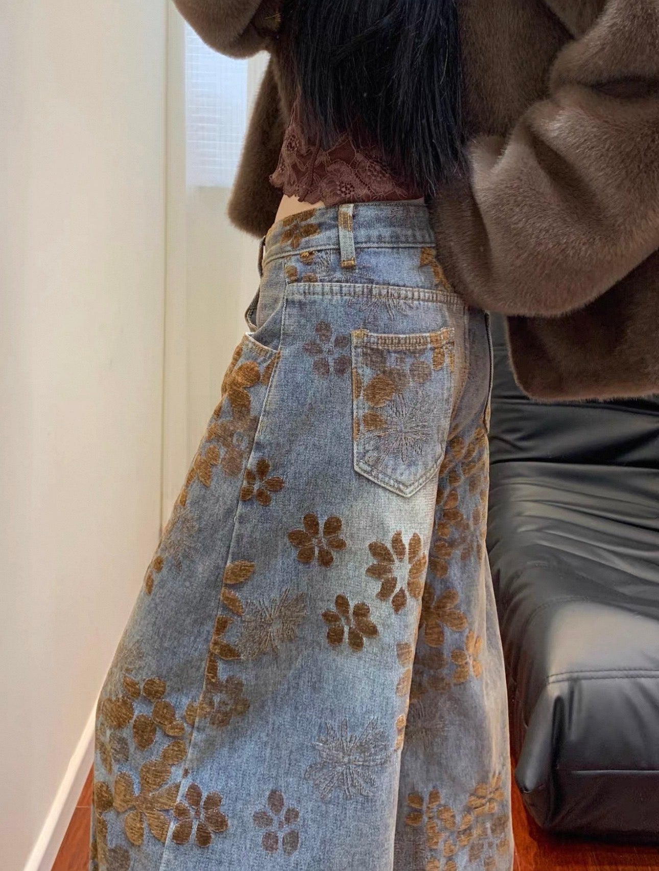 Person wearing a floral-patterned denim skirt with a brown jacket indoors.