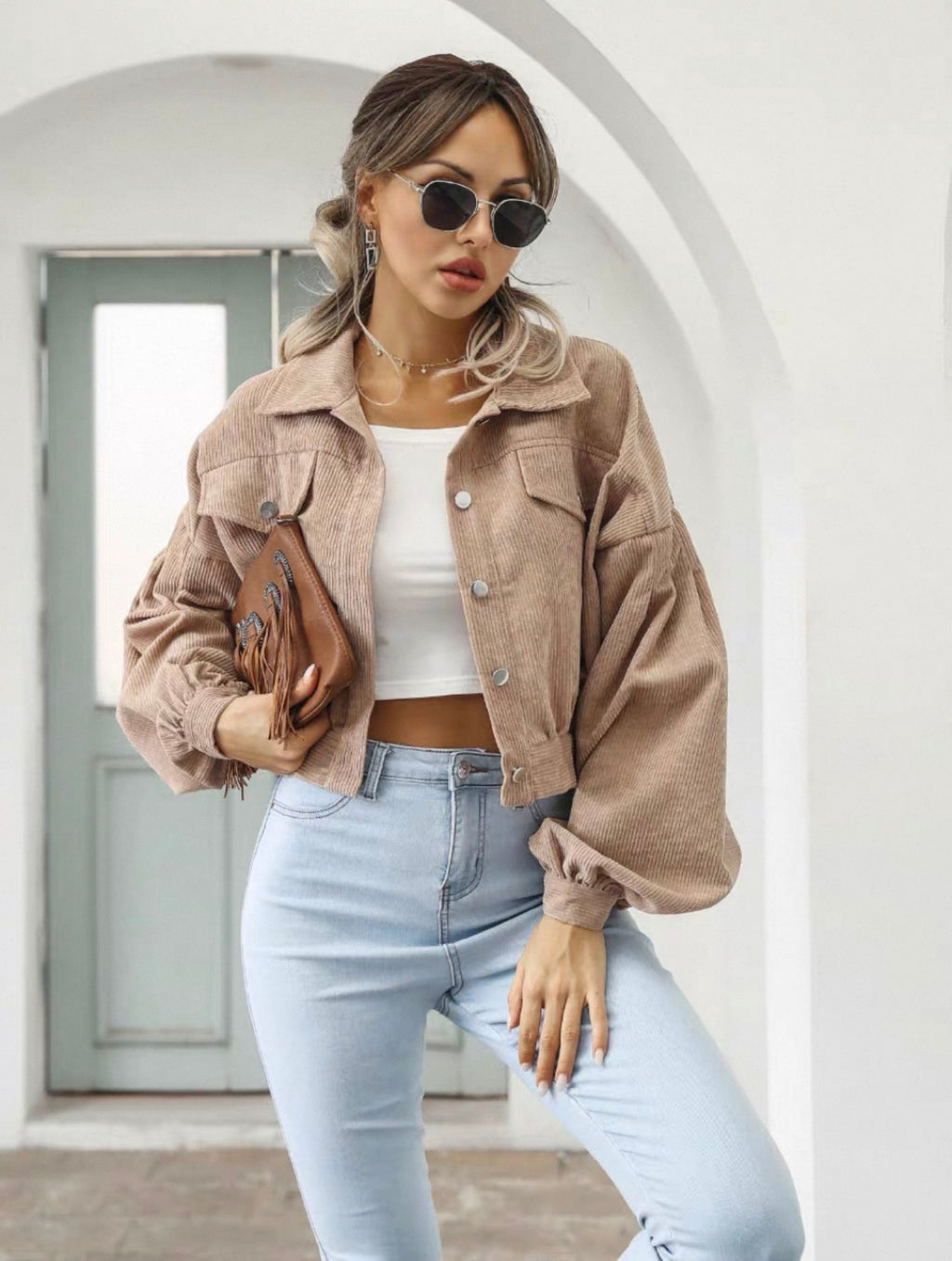 Woman wearing a beige jacket, white top, and light blue jeans with sunglasses indoors.