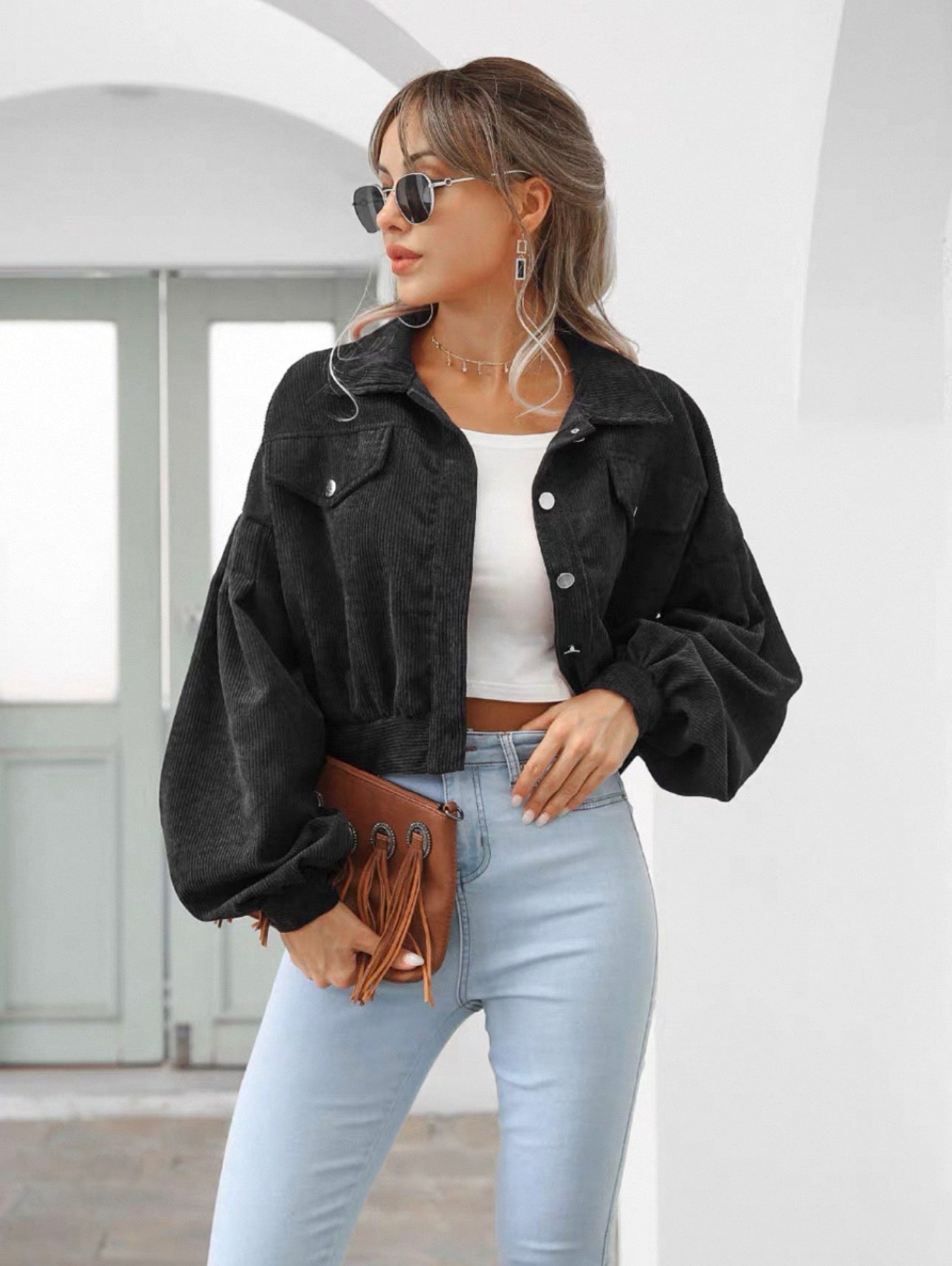 Woman wearing a black jacket, white top, and light blue jeans with sunglasses indoors.