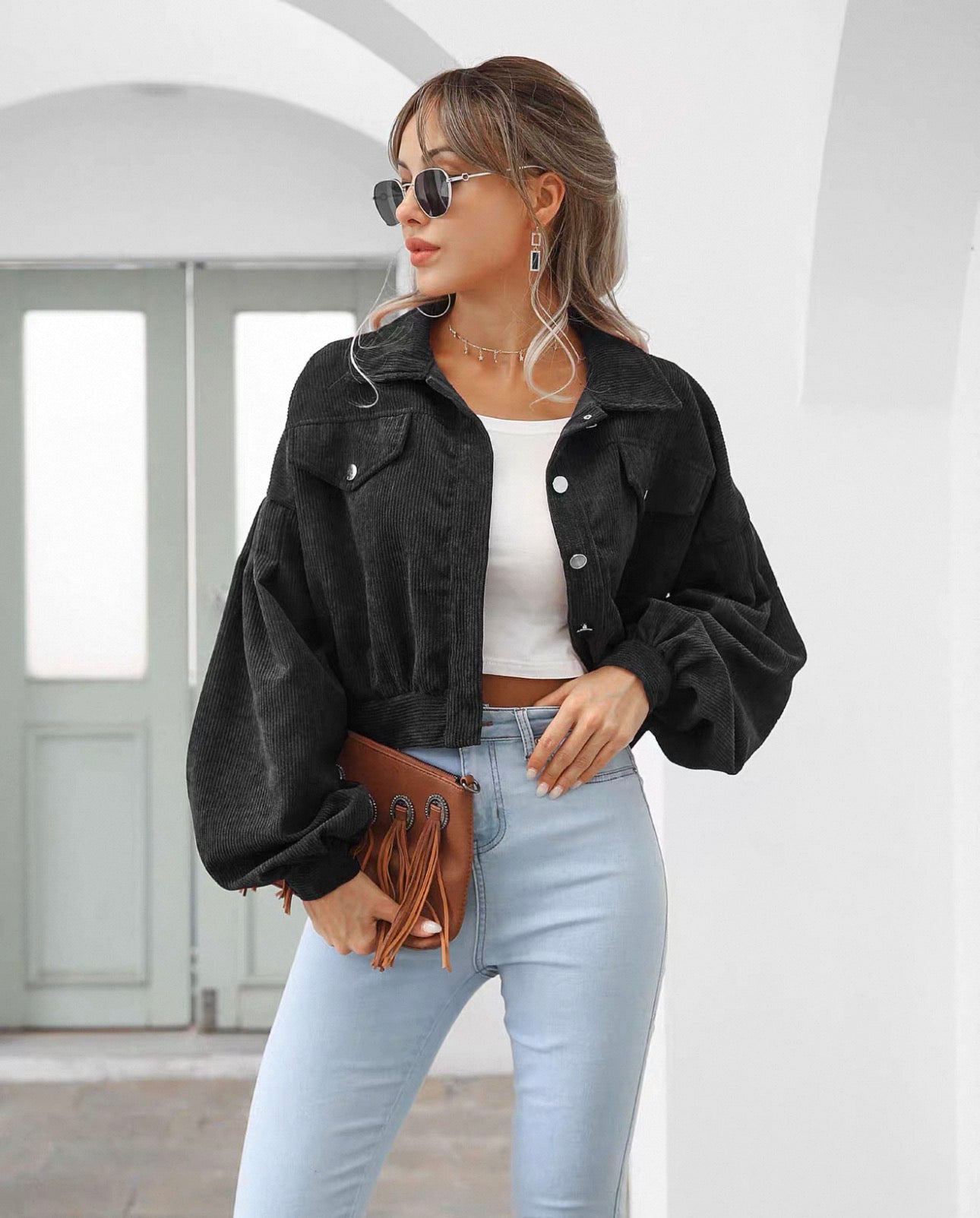 Woman wearing a black jacket, white top, and light blue jeans in an indoor setting.