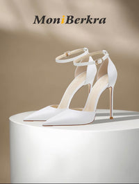 White leather stiletto heels with pointed toes and ankle straps on a curved white surface.
