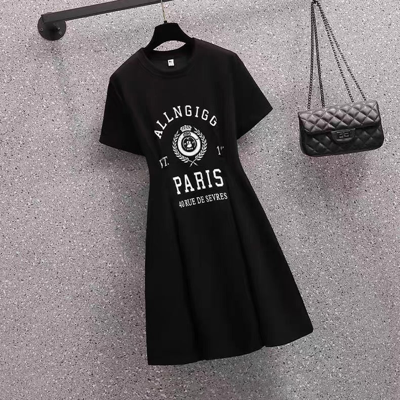 Black t-shirt with white text and graphics on a textured gray surface, next to a black handbag.