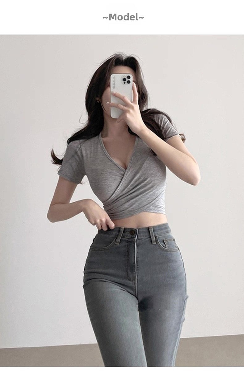Woman taking a mirror selfie wearing a gray top and high-waisted jeans.