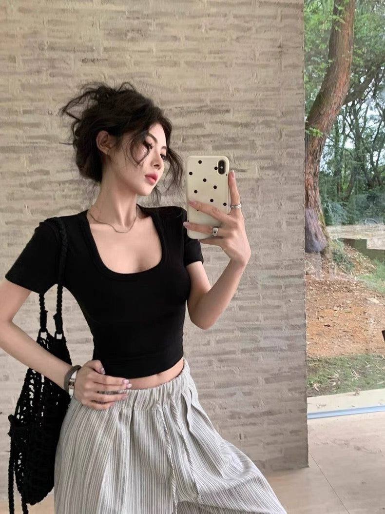 Woman taking a mirror selfie wearing a black top and light gray pants outdoors.