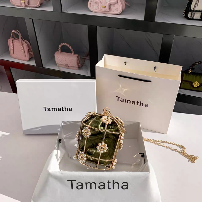 Pink handbags displayed on shelves with 'Tamatha' branded boxes and a decorative green bag on a white surface.