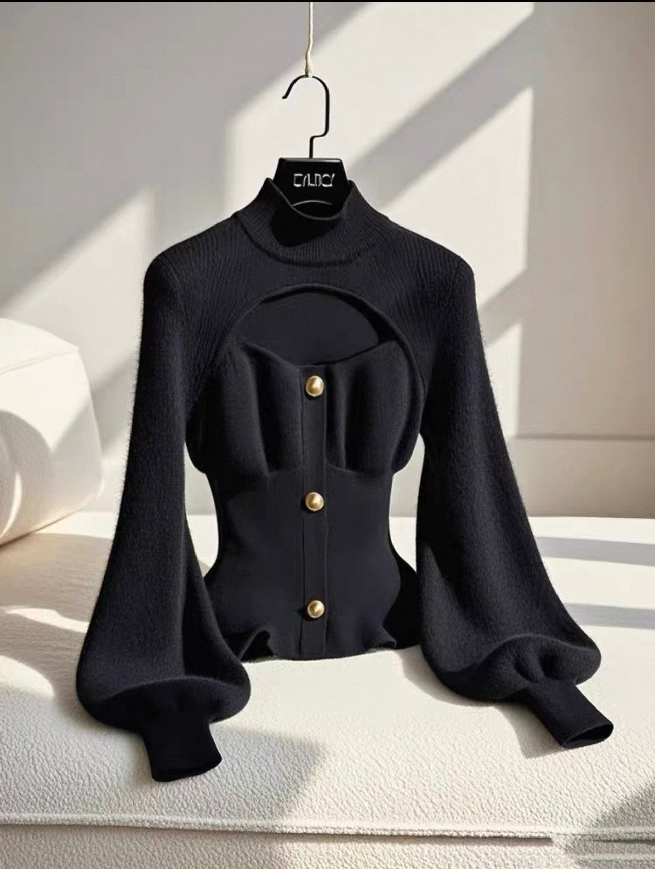 Black blouse with bell sleeves on a hanger against a neutral background