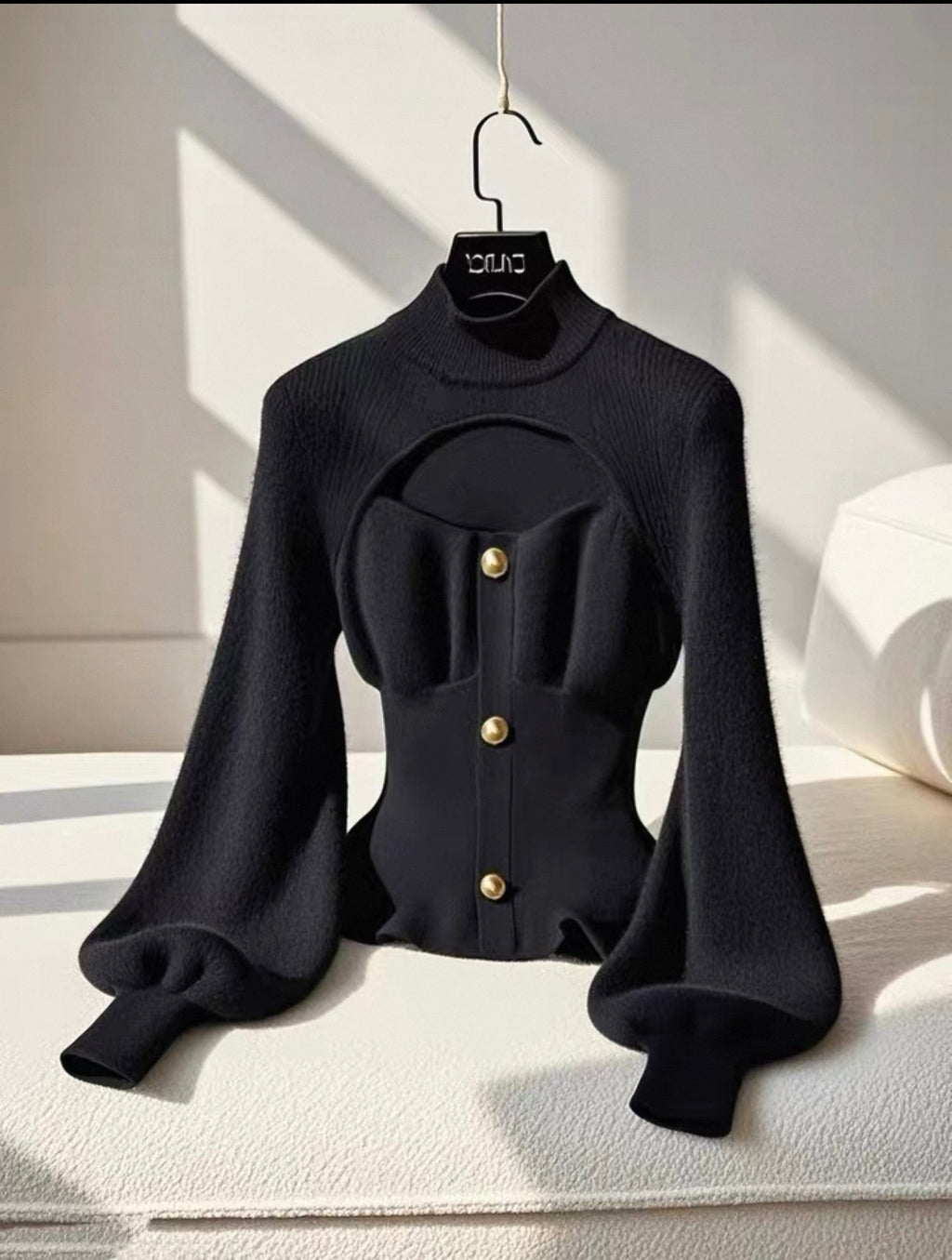 Black blouse with gold buttons on a hanger against a light background