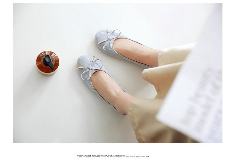 Gray flat shoes with bow details worn by a person on a white surface.