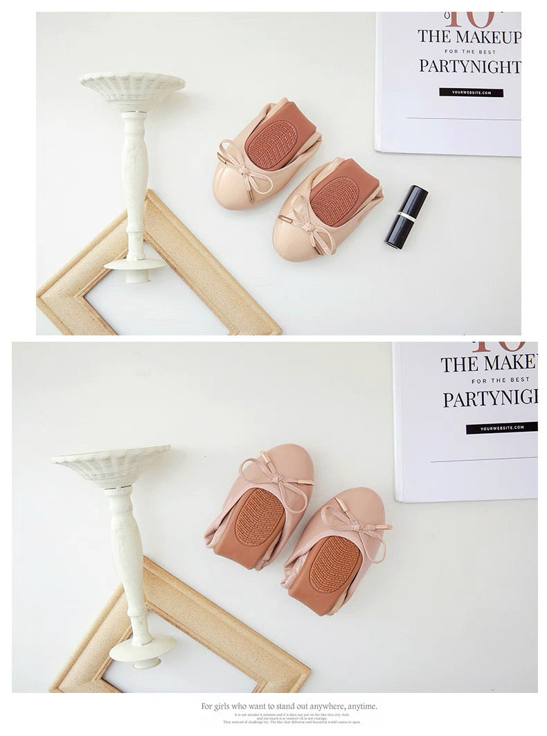 Pair of pink baby shoes with a bow on a white surface with a magazine in the background.