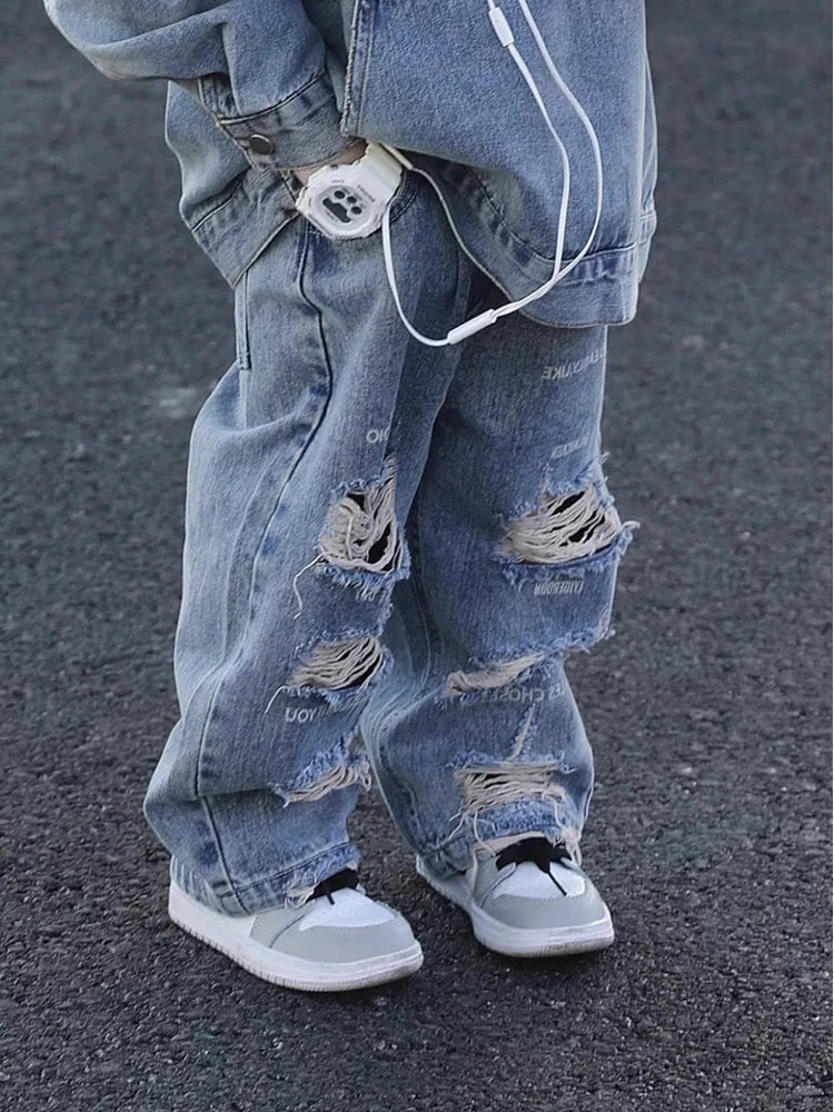 Ripped blue jeans worn by a person on a dark pavement background