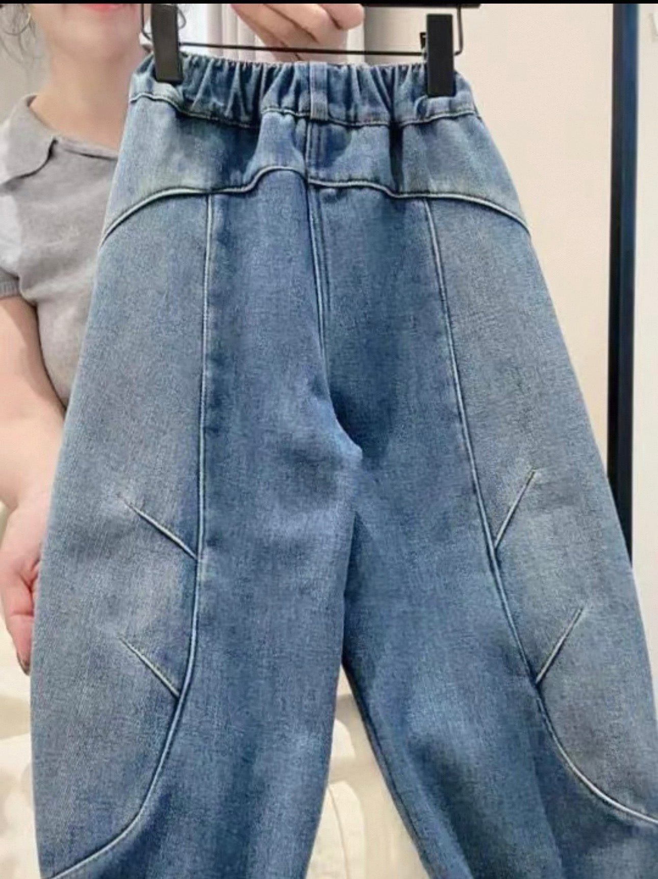 Blue denim pants on a hanger against a neutral background