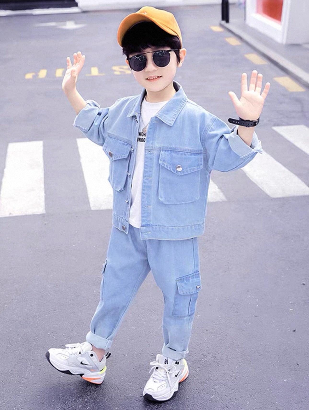 Child wearing a light blue denim outfit with sunglasses and a yellow cap on a road.