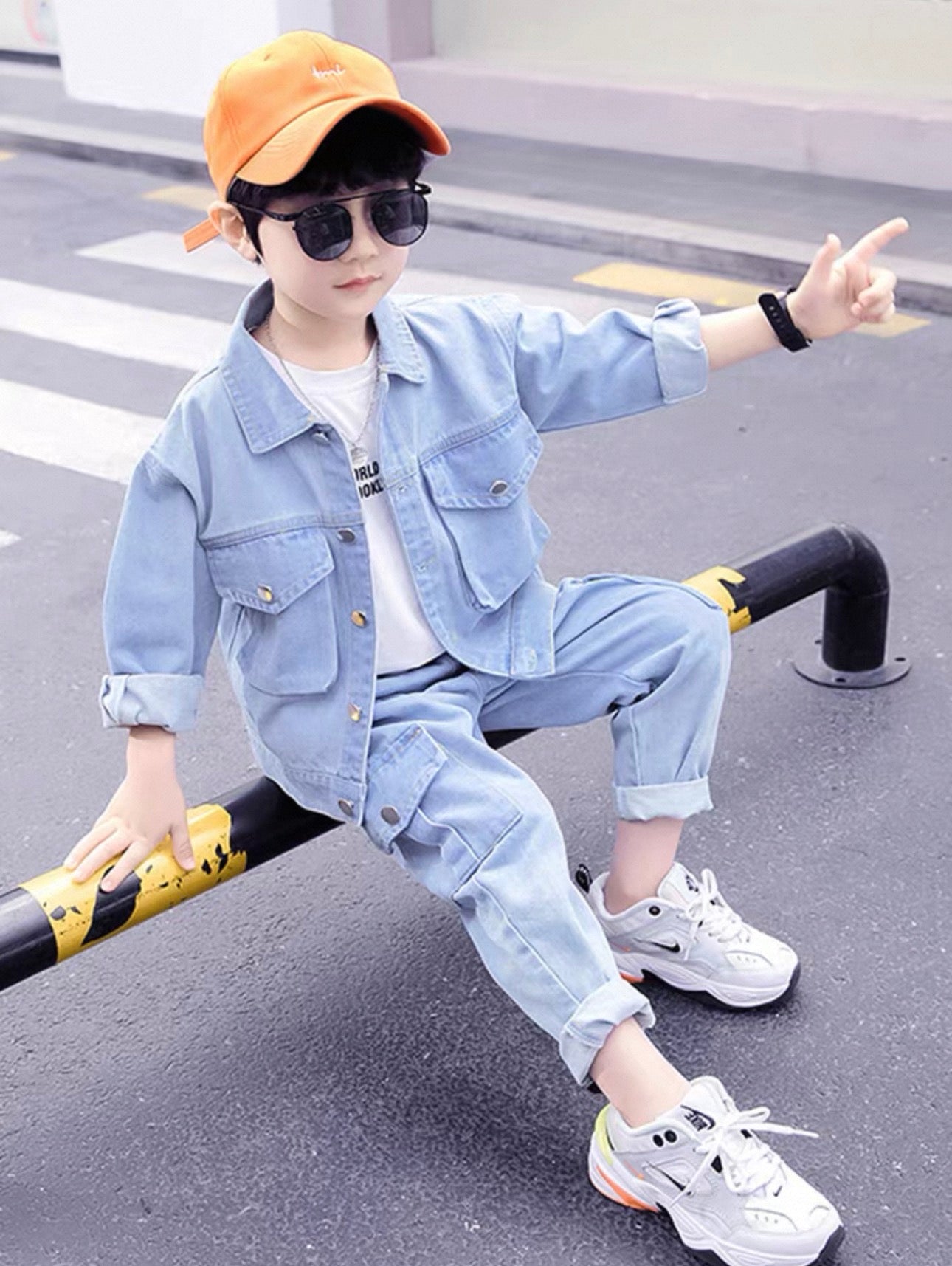 Child wearing a light blue denim outfit with a yellow cap and sunglasses, sitting on a black and yellow pole.