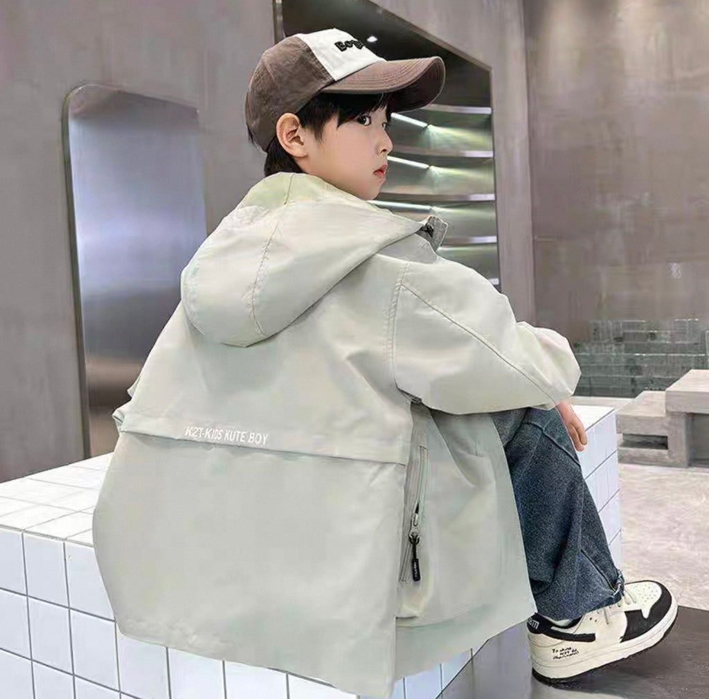 Child wearing a light-colored jacket and cap sitting on a ledge.
