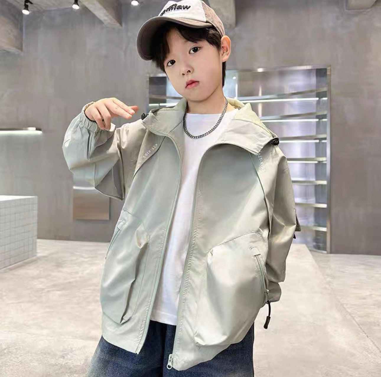 Child wearing a light gray jacket and cap indoors