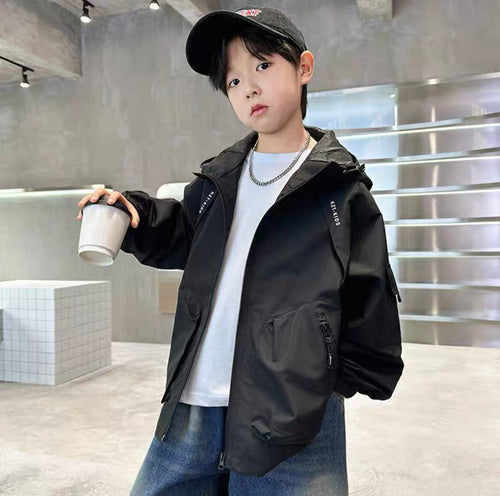 Child wearing a black jacket and cap, holding a white cup in a modern indoor setting.