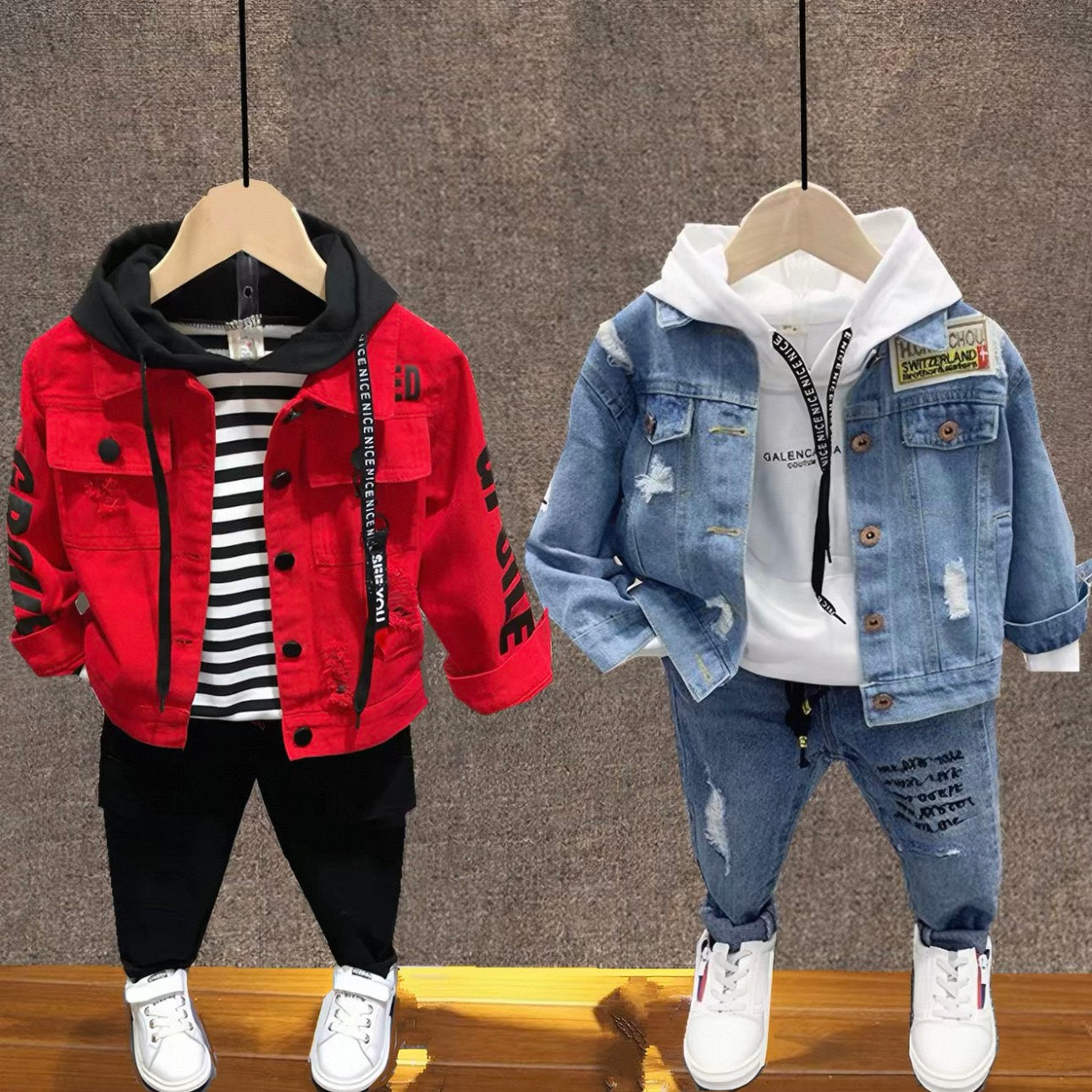 Two children's outfits on hangers against a textured wall.