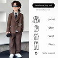 Child wearing a formal brown suit with sunglasses, standing against a light-colored wall.