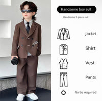 Child wearing a formal brown suit with sunglasses, standing against a light-colored wall.