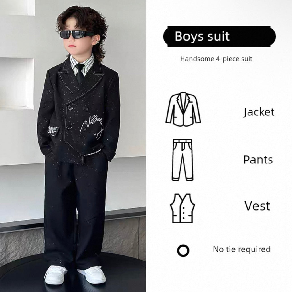 Young boy wearing a black suit with sunglasses, standing against a neutral background.