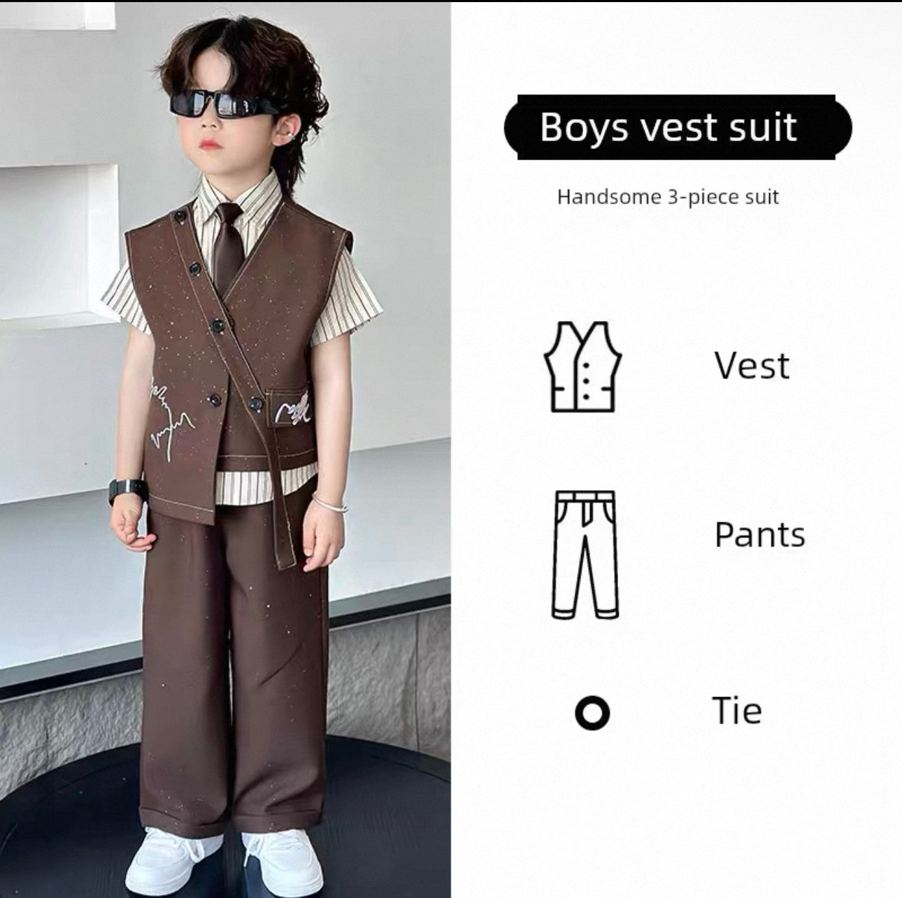 Child wearing a brown vest suit with a tie, standing against a white wall.