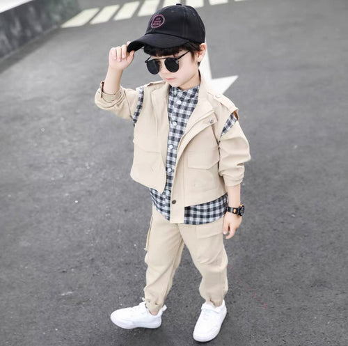 Child wearing a beige jacket, plaid shirt, and pants on a road.