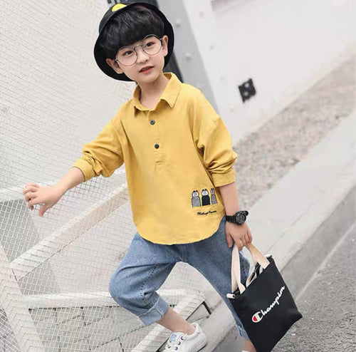 Child wearing a yellow shirt with a small design, holding a black bag with visible branding, standing on a modern staircase.