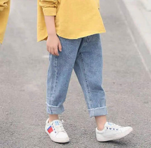 Child wearing yellow top, blue jeans, and white sneakers on a gray pavement.