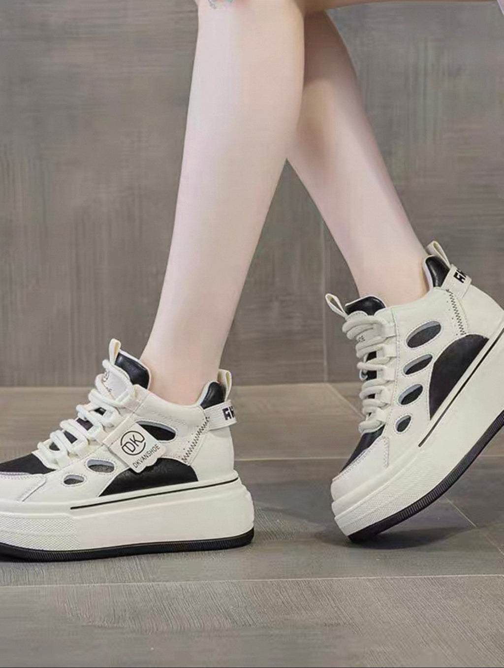 White sneakers with black accents worn by a person on a wooden floor.