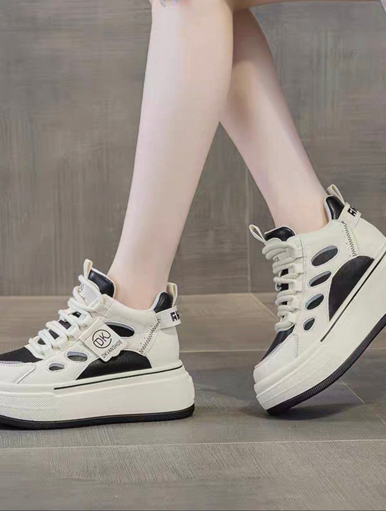 White sneakers with black accents worn by a person on a wooden floor.