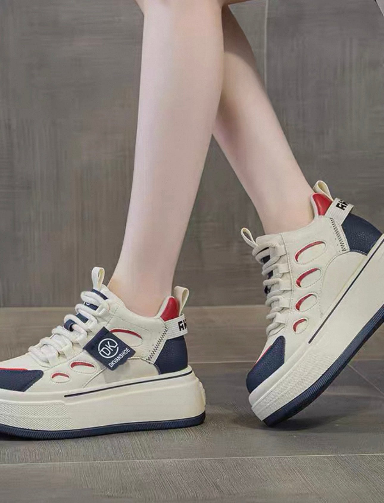 White sneakers with blue and red accents worn by a person on a gray floor.