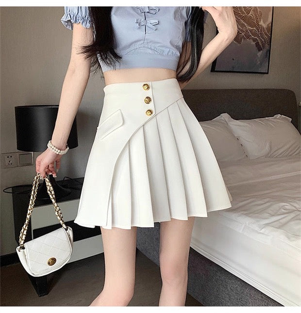 Person wearing a white pleated skirt with gold buttons in a bedroom setting