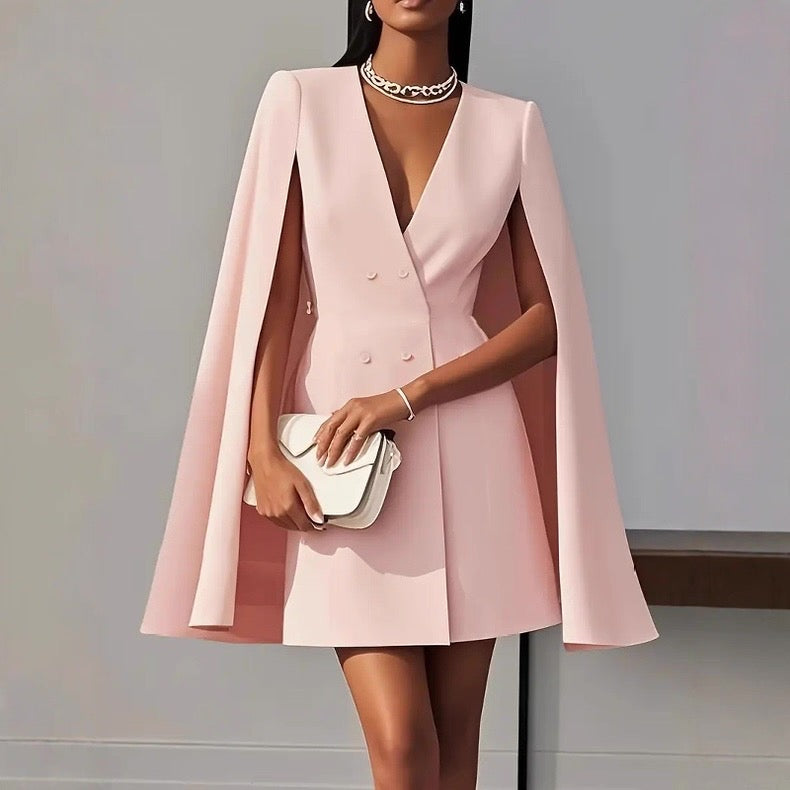 Woman wearing a pink cape dress holding a white clutch against a gray background