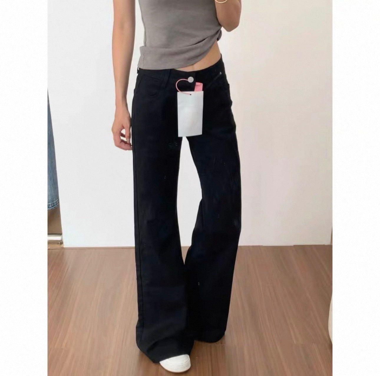 Person wearing black wide-leg jeans with a tag, standing on a wooden floor.
