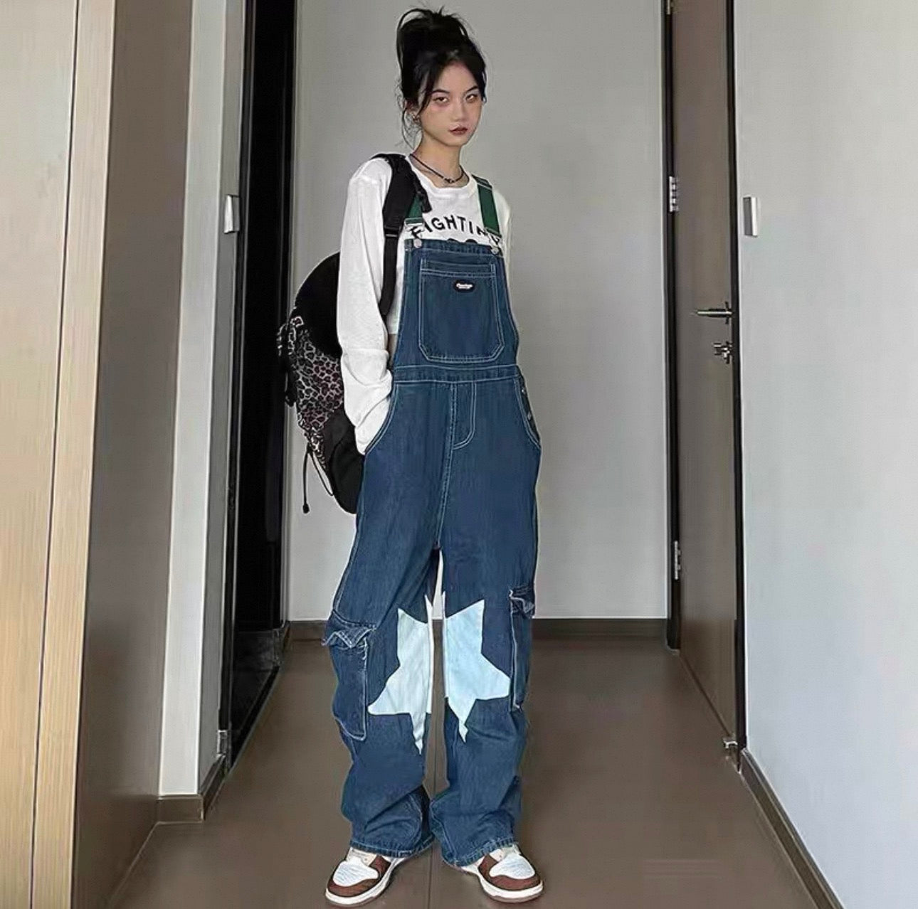 Person wearing a denim overalls with star patterns in a hallway.