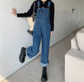 Person wearing blue denim overalls in a minimal indoor setting