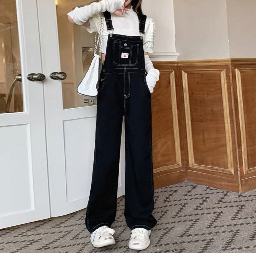 Person wearing black overalls and white sneakers in a room with wooden paneling.
