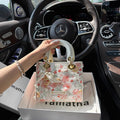 Floral handbag held by a hand in front of a car interior with a visible Mercedes logo.