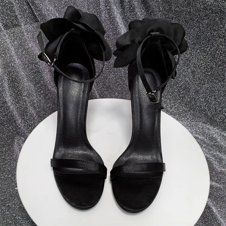Black satin stiletto heels with floral ruffle ankle straps and slim toe bands on white platform.