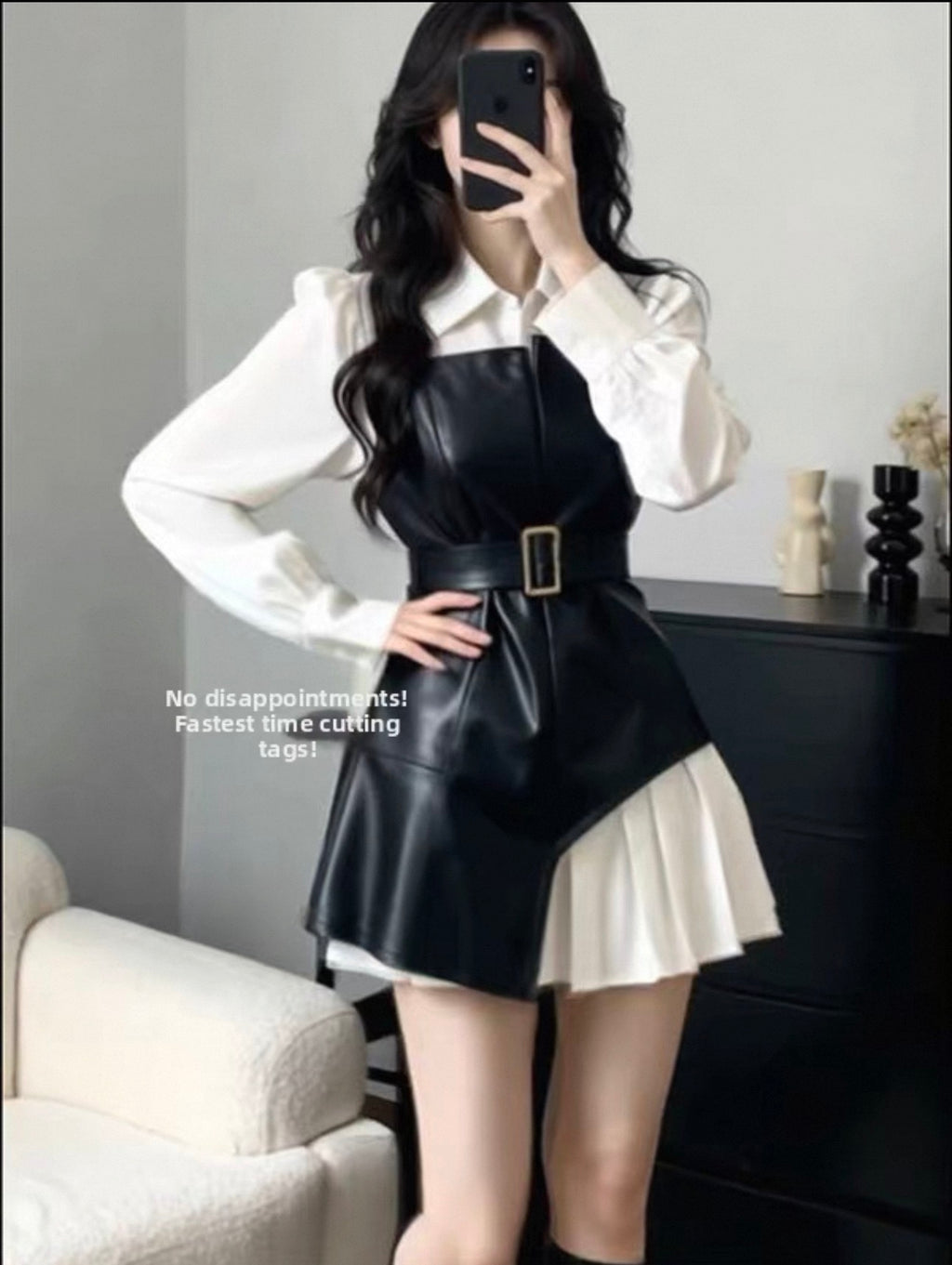 Person wearing a black leather apron over a white shirt and skirt in a room.