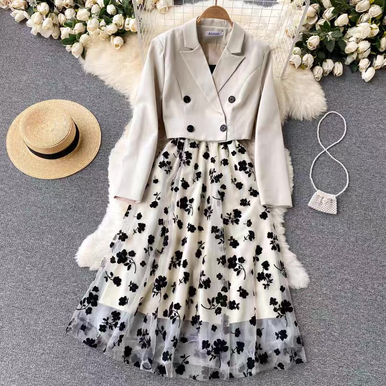White blazer with black buttons and a floral skirt on a gray surface with decorative elements.