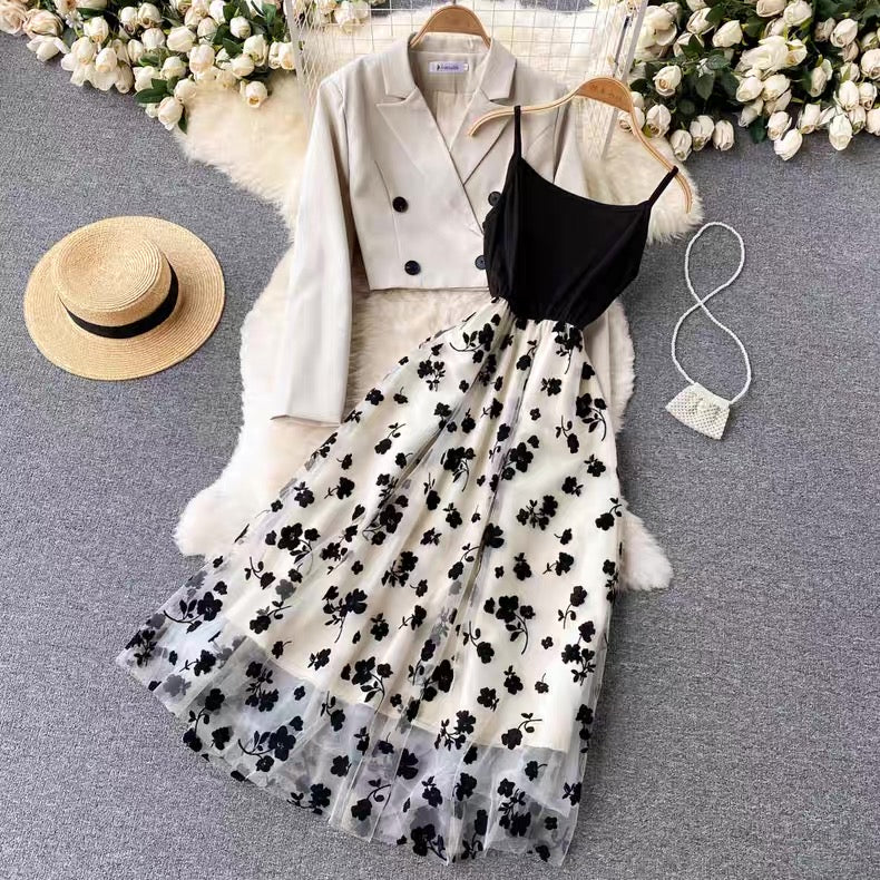 Fashion outfit with floral skirt, blazer, and hat on a textured surface with flowers in the background.