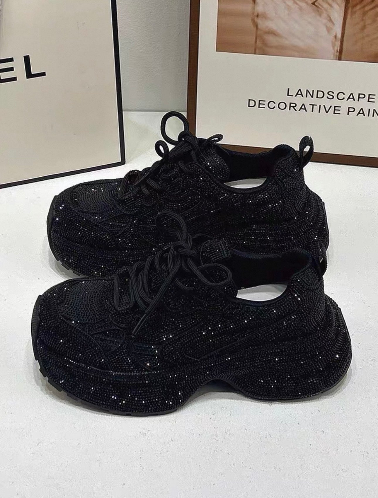 Black glittery sneakers on a white surface with blurred background