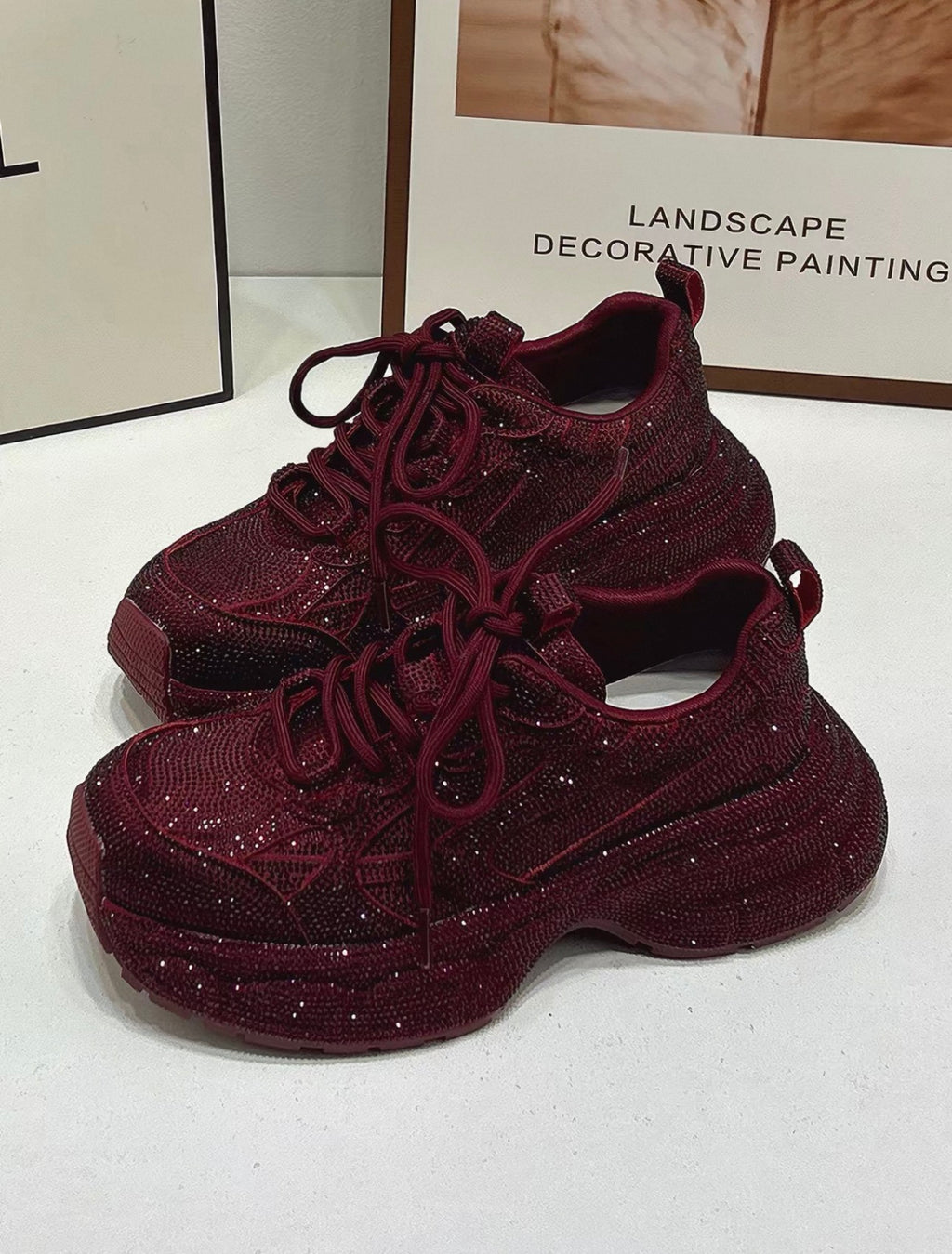Maroon glittery sneakers on a white surface with a blurred background