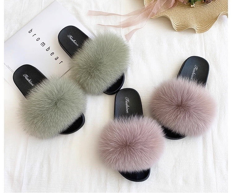 Pair of black slippers with fluffy pom-pom on a white surface